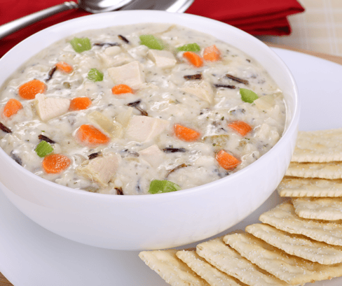A  bowl of creamy turkey soup sits on a table surrounded by crackers.