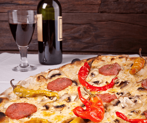 Pepperoni pizza with peppers sitting next to a glass and bottle of red wine.