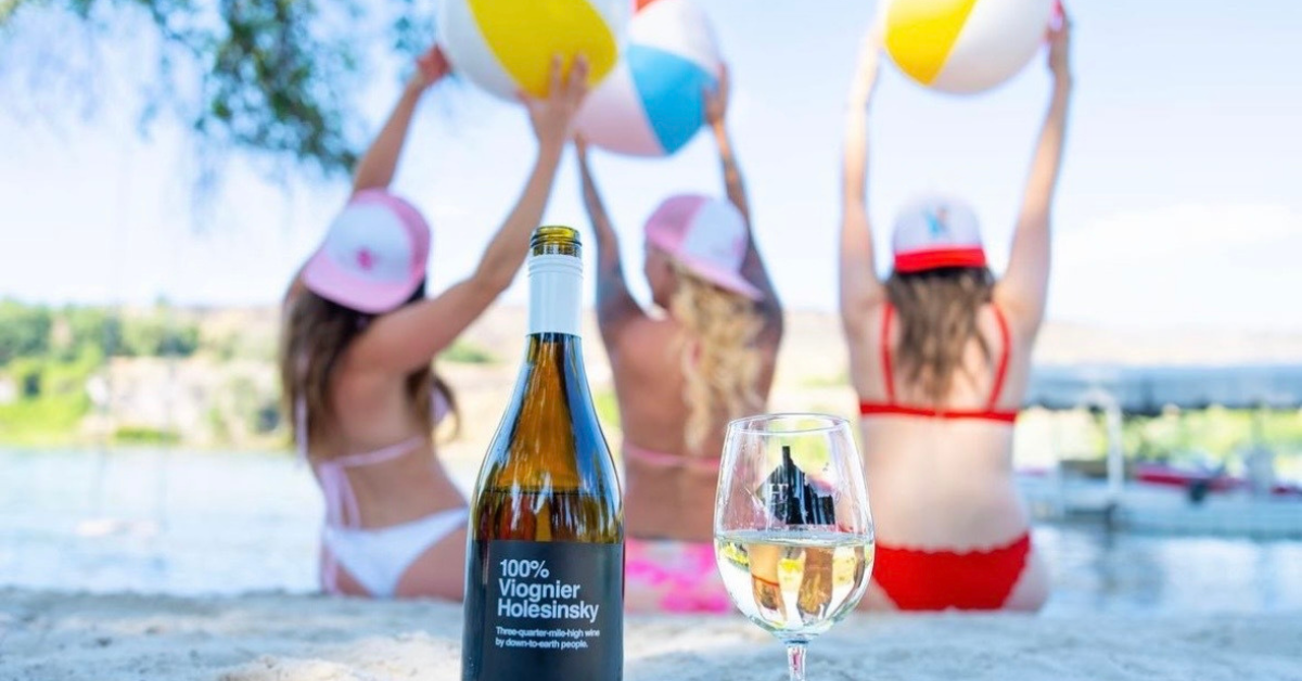 Bottle of Idaho Viognier sitting in sand in front of women holding beach balls